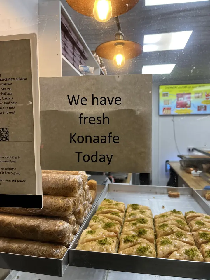Fresh kunafa sign above trays of baklava at the counter
